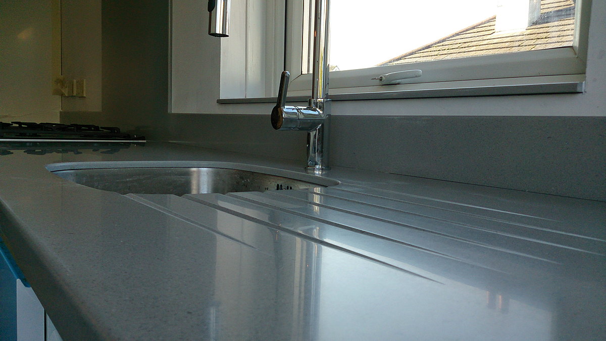 A grey solid-surface worktop with moulded drainer grooves and an undermount sink
