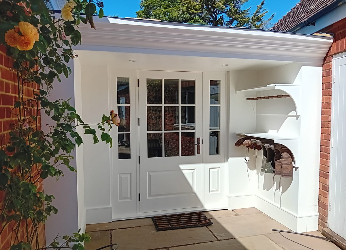 A bespoke painted back door with glazed sidelights under a new porch with a shaped cornice and fitted boot racks