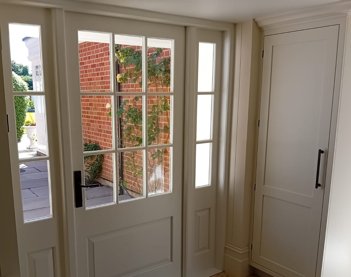 The glazed back door and sidelights seen from inside, beside a tall painted cupboard