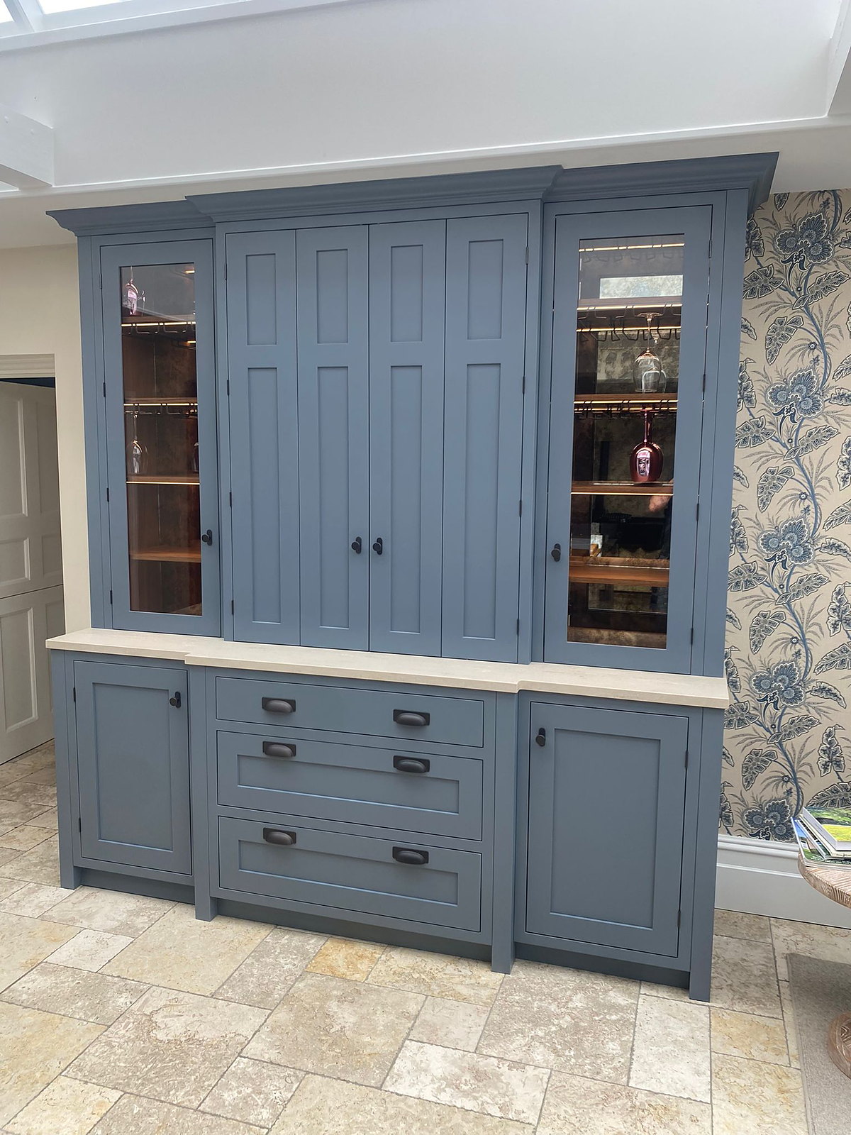 A painted blue-grey dresser with lit glazed cabinets either side of panelled doors, over drawers and cupboards