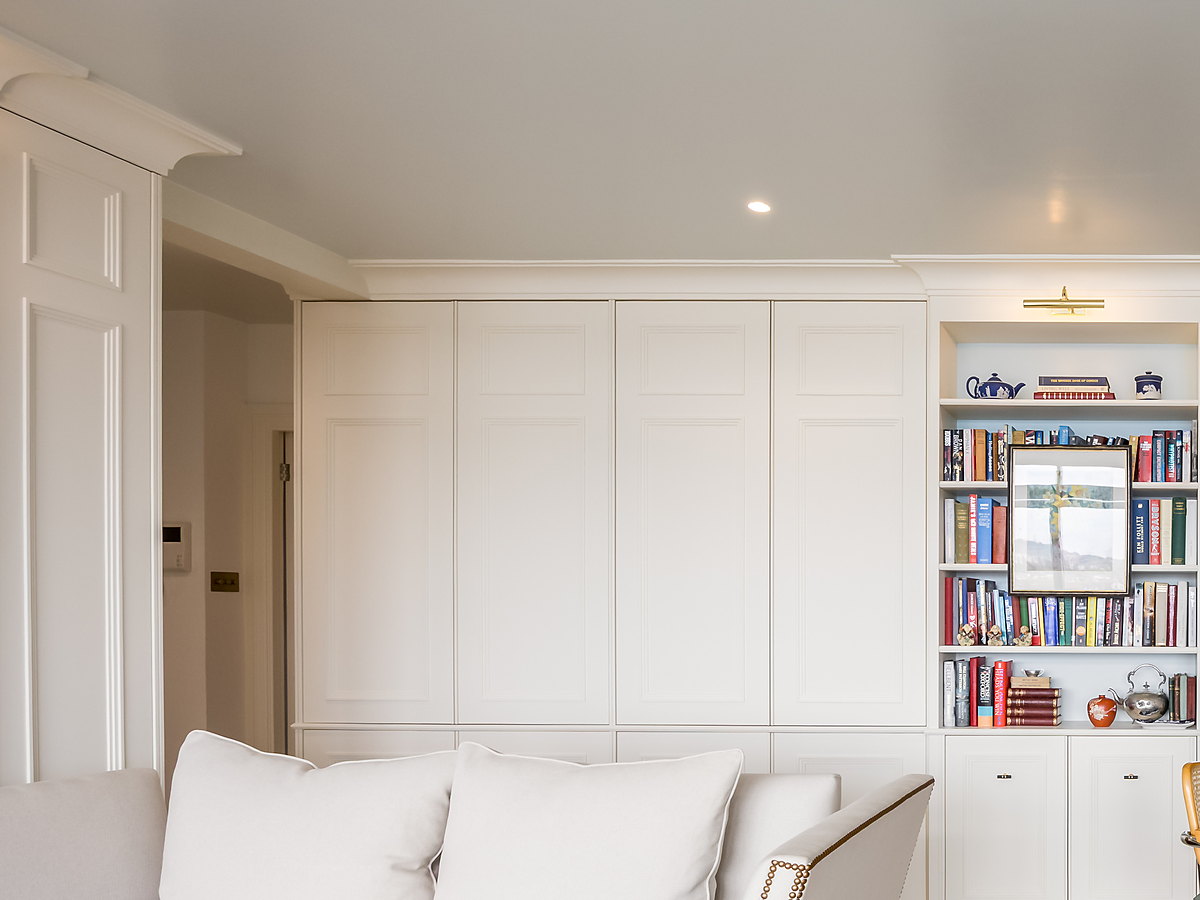 Painted full-height cupboards with panelled doors, and a bookcase with a brass picture light built in beside them