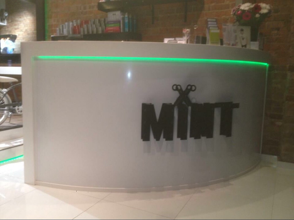 The curved white reception desk with a green light strip that MSO made for the MINT hair salon
