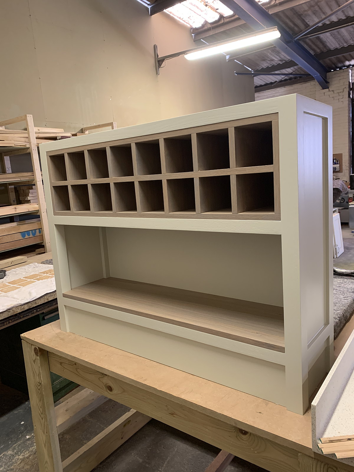 A painted wine-bin cabinet standing on a bench in the workshop